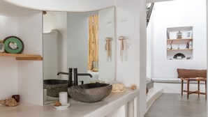Une salle de bain moderne avec un grand miroir, un lavabo en pierre et une étagère en bois agrémentée d’objets décoratifs.