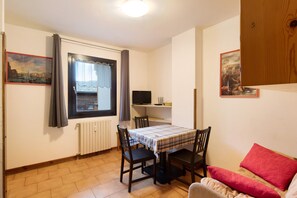 A room with a dining table, chairs, a television, a radiator, and a window with curtains.