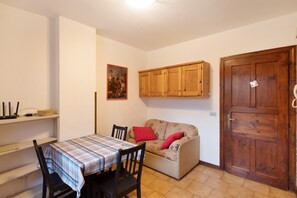 A dining area with a table set for two, a sofa with red cushions, wooden cabinets above the sofa, and a closed wooden door. - Apartment 'Residence Paradisin' with Mountain View and Wi-Fi (Livigno)