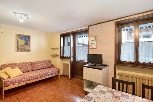 A furnished room with a sofa, a table, a TV, and a window with curtains.