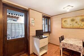 A room with a wooden door, a small desk with a computer, a dining table with chairs, and a wall with a sunflower painting.