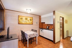 A compact kitchen with wooden paneling, a dining table with chairs, a microwave, and a sink.