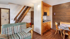 Un espacio habitable compacto con sofá, mesa de comedor de madera, área de cocina y una escalera.