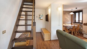Una escalera lleva a un dormitorio en el altillo, un comedor con mesa y sillas, y un sofá verde en la sala de estar.