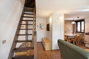 A staircase leading to a loft bedroom, a dining area with a table and chairs, and a green sofa in a living space.