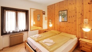 A room with wooden paneling, two beds with towels, a window with curtains, and wall-mounted lights.