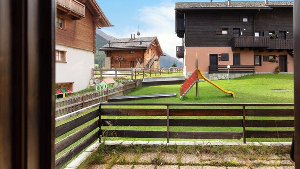 A wooden building with a balcony, a playground with a slide, and a fenced area.