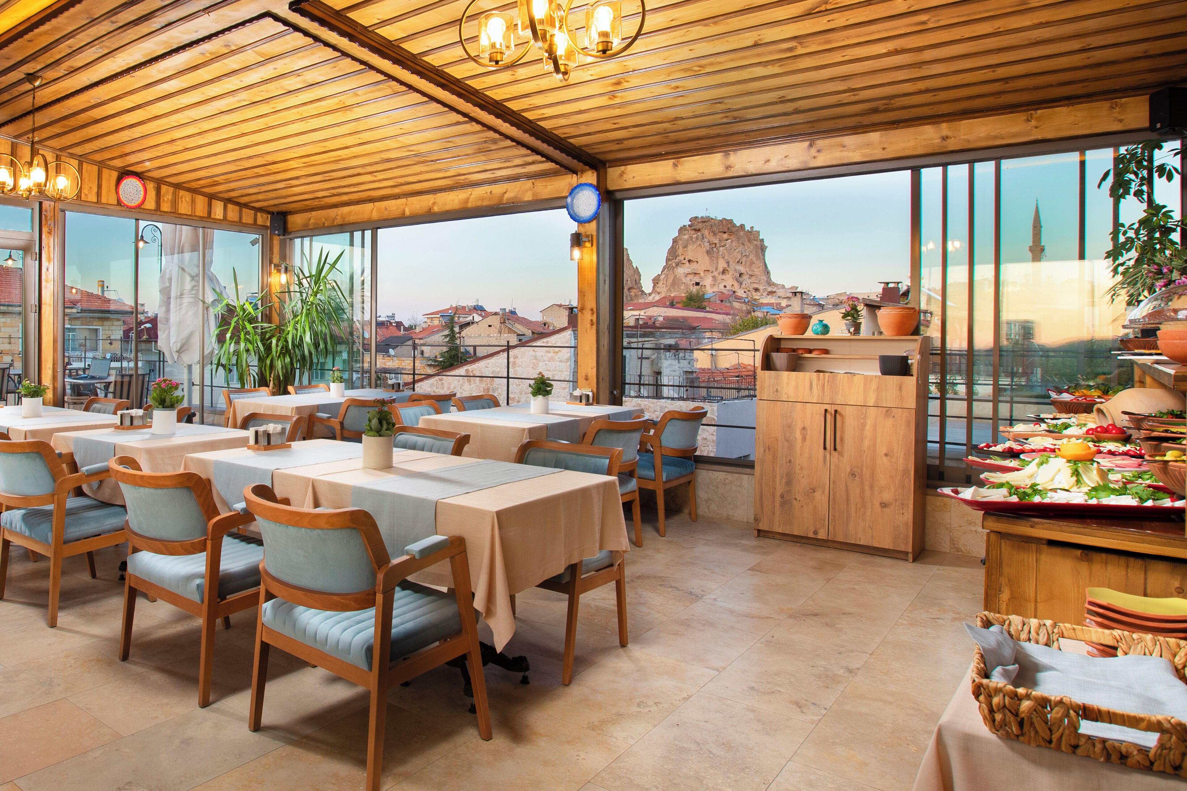 A restaurant with wooden tables and chairs, large windows, and a view of a mountain.