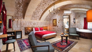 A stone-walled bedroom with a bed, a chair, a small table, and a bathtub. - Woox Cappadocia Hotel (Nevsehir)