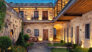 A stone building with a covered patio, a wooden door, and a small garden with flowers and shrubs. - Woox Cappadocia Hotel (Nevsehir)