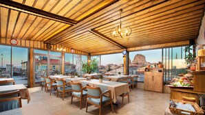 A restaurant with wooden tables and chairs, large windows, and a view of a mountain. - Woox Cappadocia Hotel (Nevsehir)