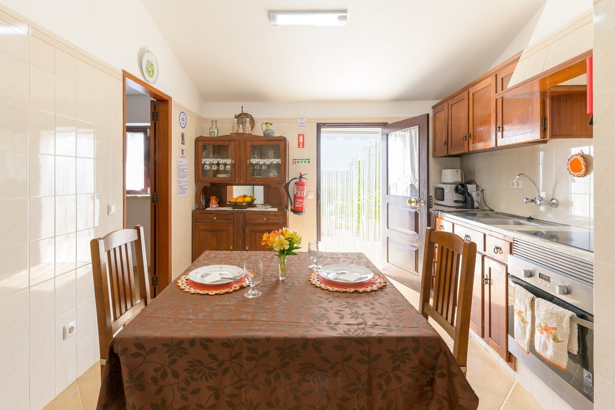 Comedor con una mesa dispuesta para dos, cocina con electrodomésticos modernos y vista a través de una puerta.