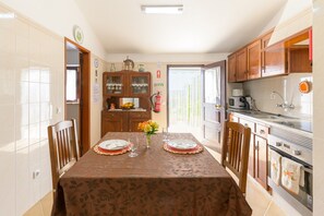 A dining area with a table set for two, a kitchen with modern appliances, and a view through a door.