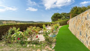 A landscaped garden with a stone wall, green lawn, and various plants. - Vacation Home "Bela Casa Na Costa Vicentina" with Private Pool, Private Garden & Wi-Fi (Aljezur)