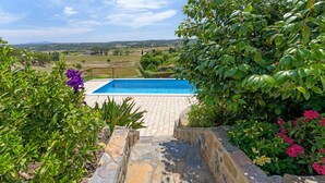 A stone pathway leading to a swimming pool surrounded by lush greenery and a scenic view of rolling hills. - Vacation Home "Bela Casa Na Costa Vicentina" with Private Pool, Private Garden & Wi-Fi (Aljezur)