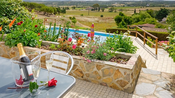 A patio with a stone wall, a glass table, a bottle of champagne, and a rose. - Vacation Home "Bela Casa Na Costa Vicentina" with Private Pool, Private Garden & Wi-Fi (Aljezur)