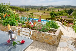 A patio with a stone wall, a glass table, a bottle of champagne, and a rose.