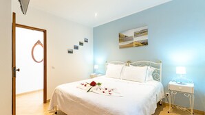 A neatly made bed with a white bedspread and a single red rose, a bedside table with a lamp, and a wall-mounted picture. - Vacation Home "Bela Casa Na Costa Vicentina" with Private Pool, Private Garden & Wi-Fi (Aljezur)