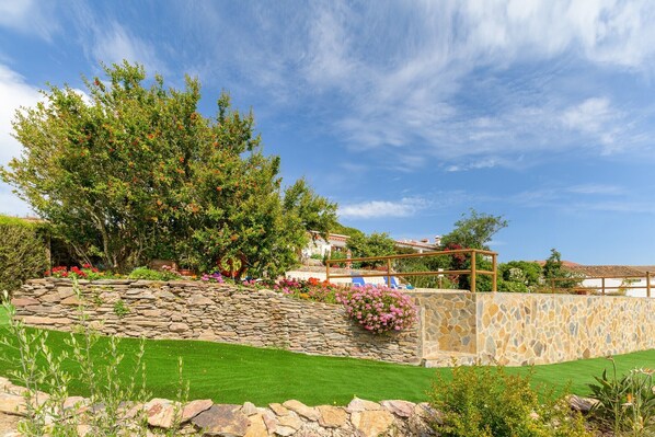 A landscaped garden with a stone wall, a wooden pergola, and a large tree.