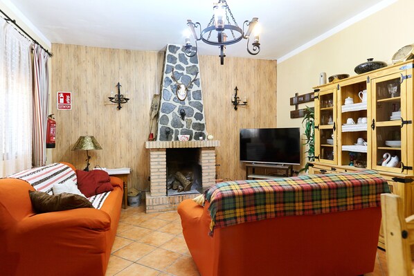 A living room with a fireplace, two sofas, a television, and a wooden cabinet with glass doors.