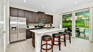 Una cocina moderna con un refrigerador de acero inoxidable, un microondas y una isla grande con taburetes de bar.
