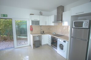 A modern kitchen with white cabinets, a microwave, a refrigerator, a washing machine, and a sink.