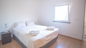 Ein Schlafzimmer mit Bett, Nachttischen, einem Fenster und einer Tür.