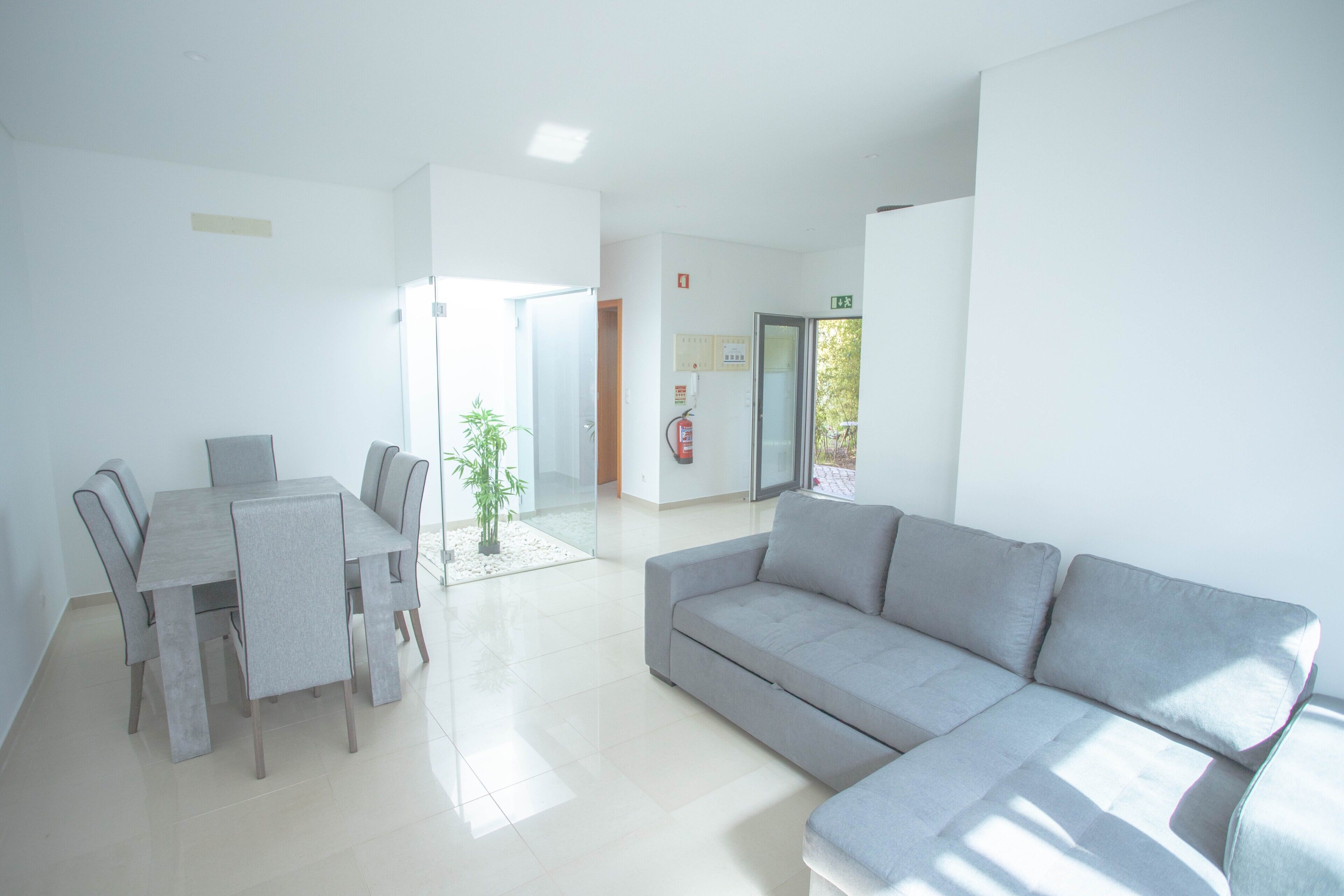 A modern living room with a grey sofa, a dining table with chairs, and a small potted plant.