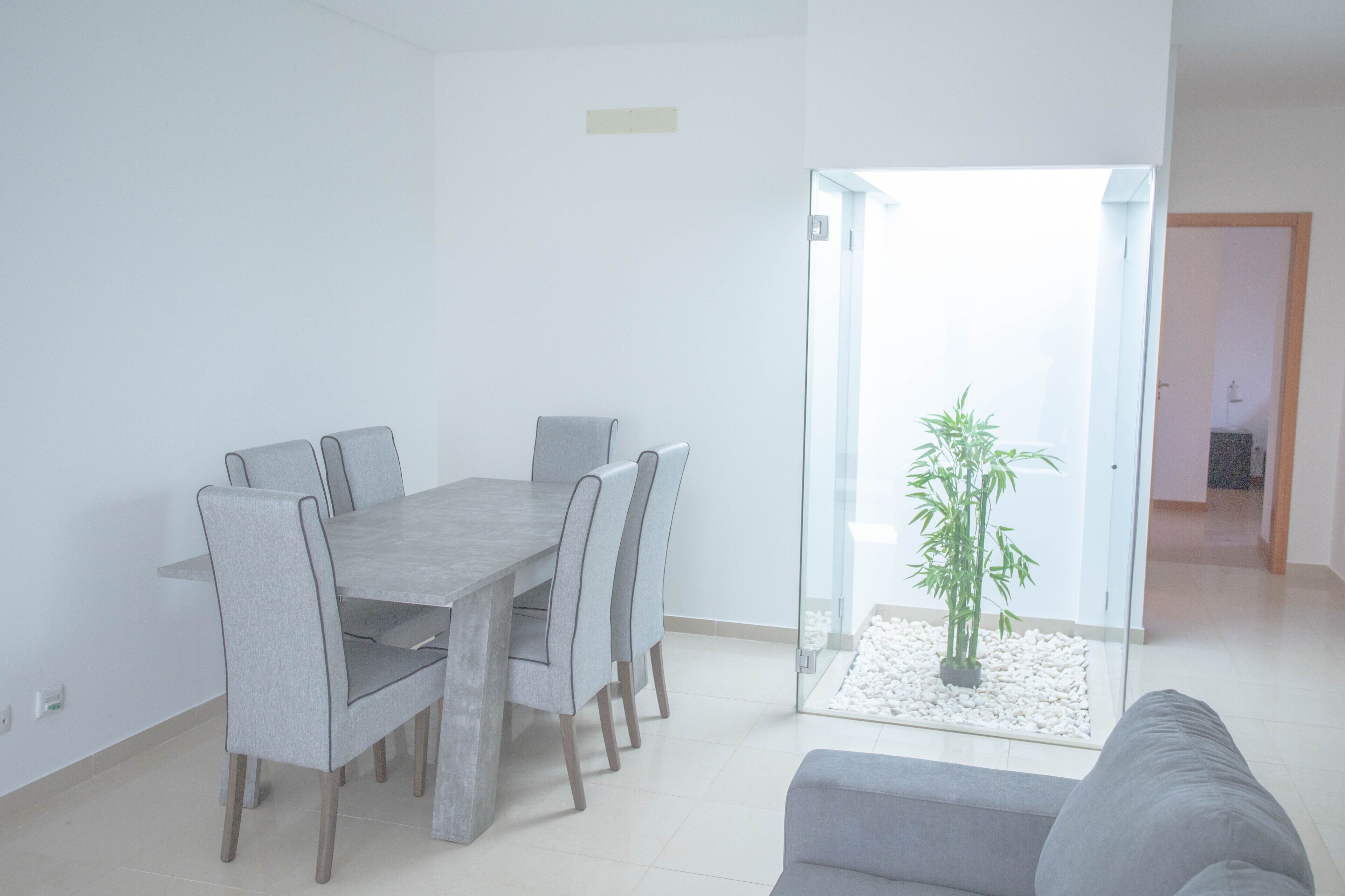 Una sala de estar moderna con comedor, puerta de vidrio que da a un balcón y un sofá gris.