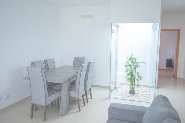 A modern living room with a dining area, a glass door leading to a balcony, and a grey sofa.