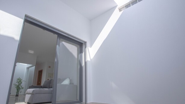 Ein modernes Zimmer mit einer Schiebeglasdoor zum Balkon, Holzboden und weißer Wand.