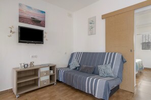 Una habitación con un sofá a rayas, un televisor montado en la pared, un mueble de madera y una puerta que da a otra estancia.