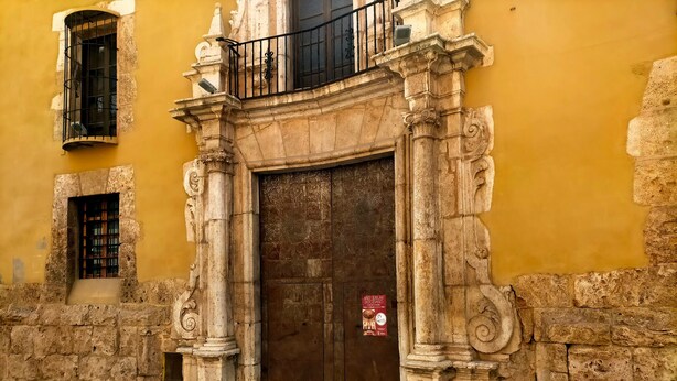 A historic building with a large wooden door, stone columns, and a small balcony with a black railing. - Vacation Home "Ca Josep" with Private Terrace, Balcony & Wi-Fi (Segorbe)