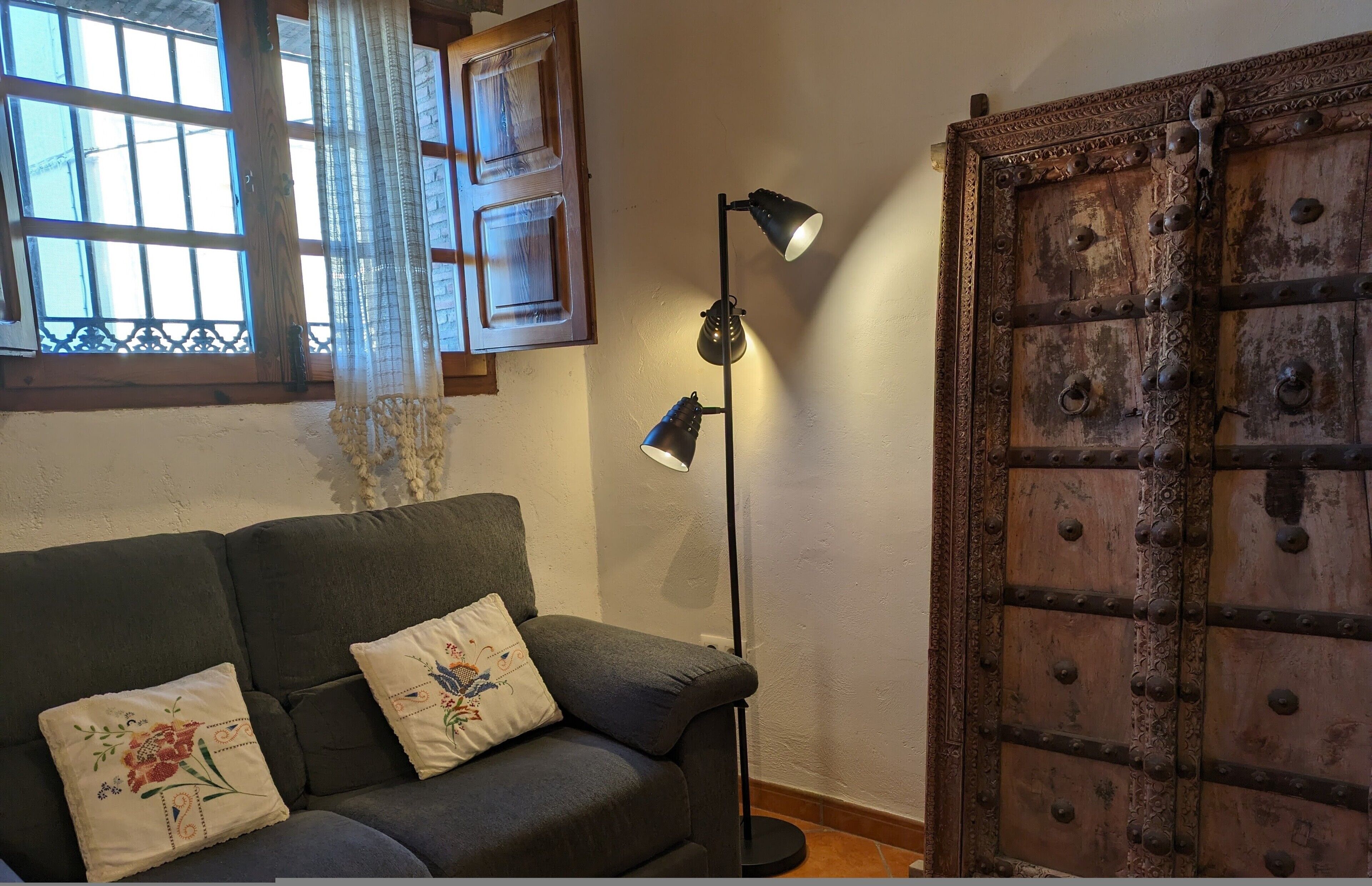 Ein Zimmer mit einer Couch, einer Stehlampe, einer Holztür und einem Fenster mit Vorhängen.