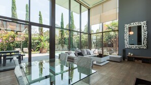 Un intérieur moderne avec une table à manger en verre, des sièges rembourrés et une vue sur l’extérieur.