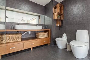 A modern bathroom with a large mirror, a wooden vanity, a white sink, a bidet, and a toilet.