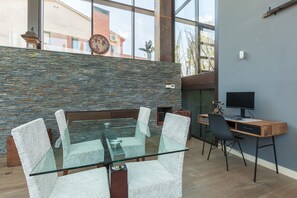 A modern interior with a glass-top table, woven chairs, a stone wall, a fireplace, and a computer desk.