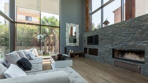 Un salon moderne avec une cheminée en pierre, de grandes fenêtres et un canapé d’angle.