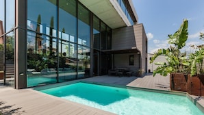 Un espace piscine extérieur moderne, doté d’une terrasse en bois, de grandes baies vitrées et d’un patio avec mobilier d’extérieur.