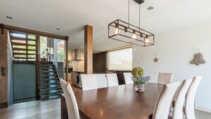 Un coin repas avec une table en bois, des chaises blanches et un luminaire suspendu.