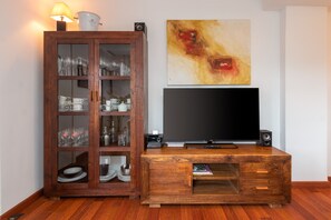 Un mueble de madera con puertas de vidrio que contiene cristalería y un televisor de pantalla plana sobre un pedestal de madera.