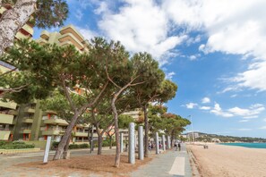 A coastal hotel with a beach view, a pedestrian walkway lined with trees, and a clear sky. - Apartment 'Maria Beach' with sea view, Wi-Fi and air conditioning (castell-Platja d´Aro)