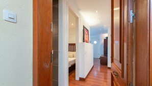 A hallway with wooden flooring, a bed in the background, and a door on the right. - Maria Beach Apartment with Sea View, Wi-Fi, and Air Conditioning (castell-Platja d´Aro)