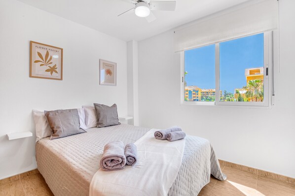 A bedroom with a bed, pillows, a window with a view, and wall art.