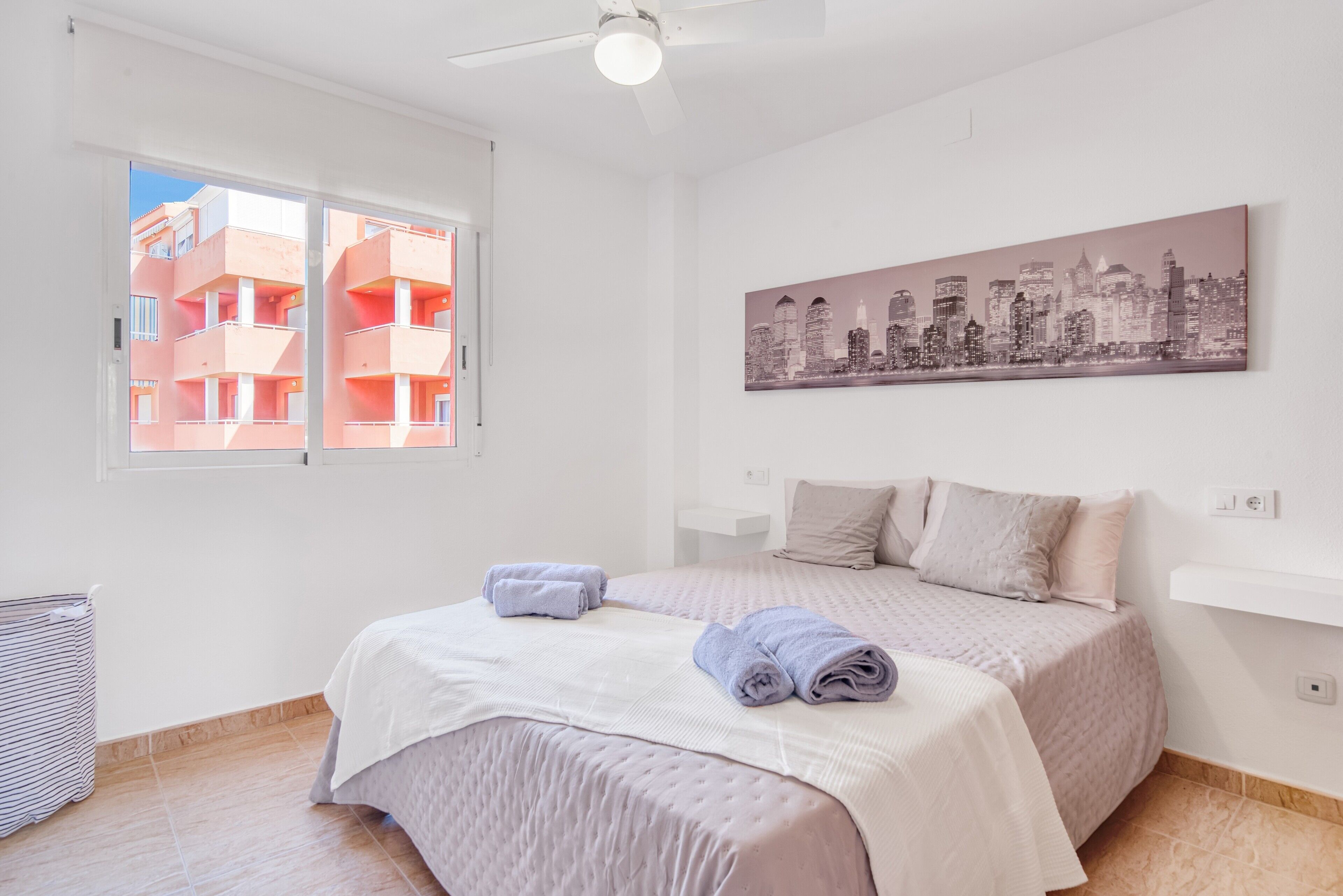 Un dormitorio con cama, un cuadro de paisaje urbano, una ventana y un radiador.