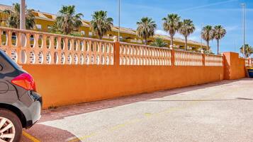 A parking area with a yellow wall and palm trees.