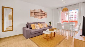 En moderne stue med sofa, rundt bord, spejl og udsigt udad.