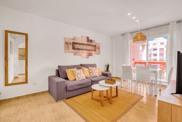 A modern living room with a sofa, a small round table, a mirror, and a view of the outside.