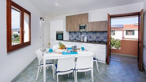 A modern kitchen with white cabinets, a microwave, and a dining area with a white table and chairs. - Holiday Home "Casa Michela" with 2 Balconies and Wi-Fi (Orosei)
