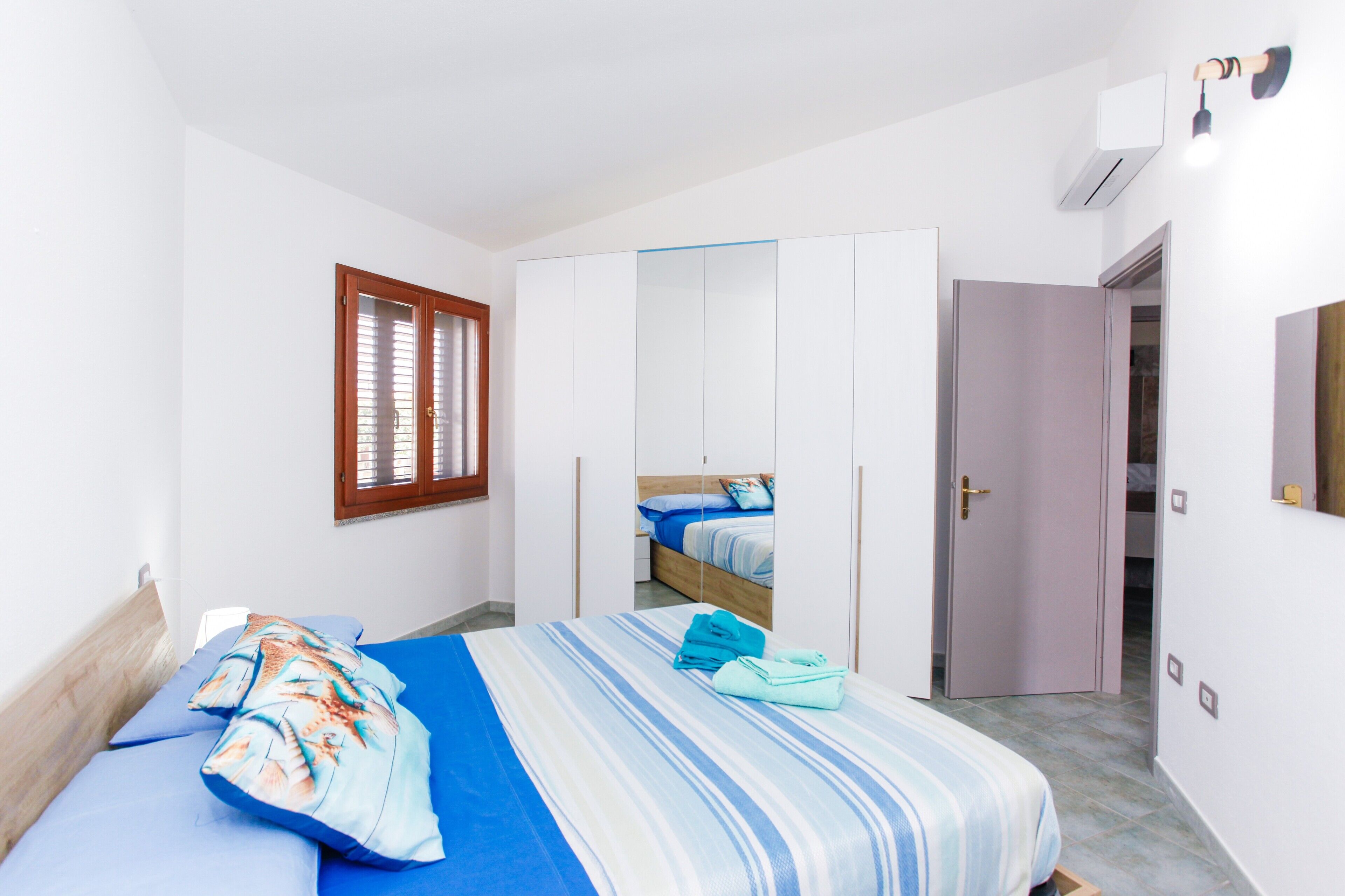 Une chambre à coucher avec un lit, une armoire, un miroir et une fenêtre avec des stores.